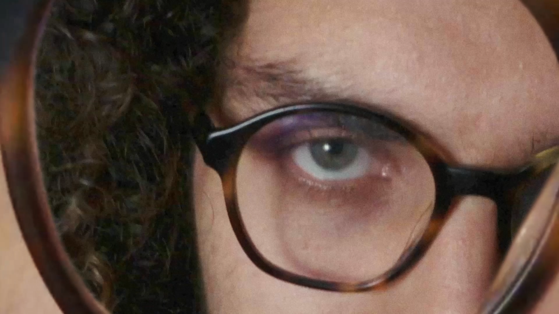 Visual parcial da cara de um rapaz com óculos castanhos escuros. No espaço que devia ser o vidro dos óculos tem uma visão repetida da própria imagem.